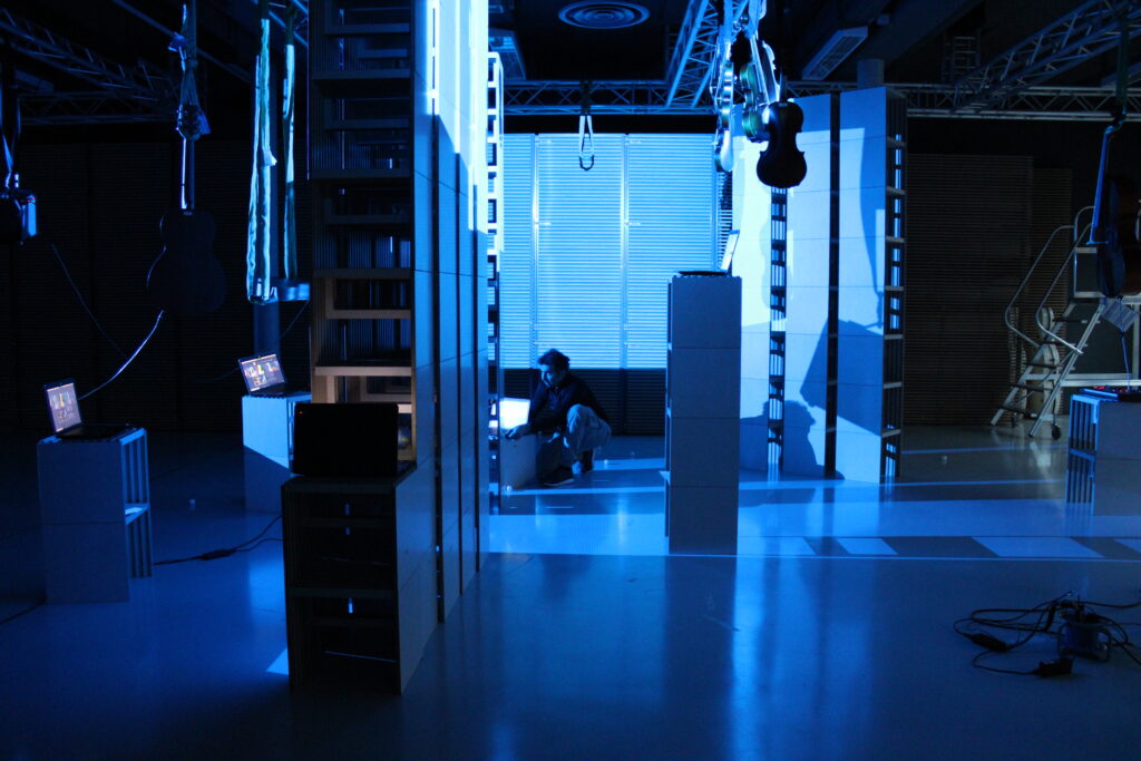 Eine Zoomsitzung mit Rochus Aust, dem Artist der Residence ,Digitale Irritationen‘. Instrumente hängen von der Decke und sind blau beläuchtet