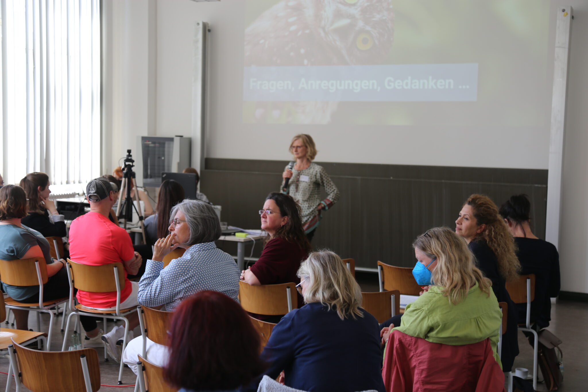 Susanne Eggert steht mit einem Mikrofon vor einem Publikum, welches sich umdreht und eine Person hinten anschaut